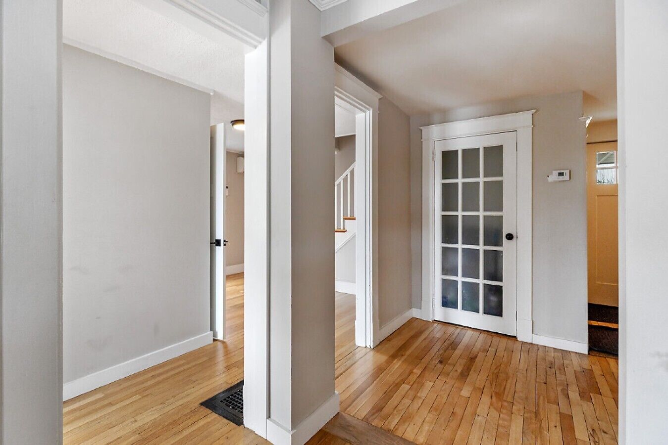 A hallway with wooden flooring, white walls, and a door with frosted glass panels.