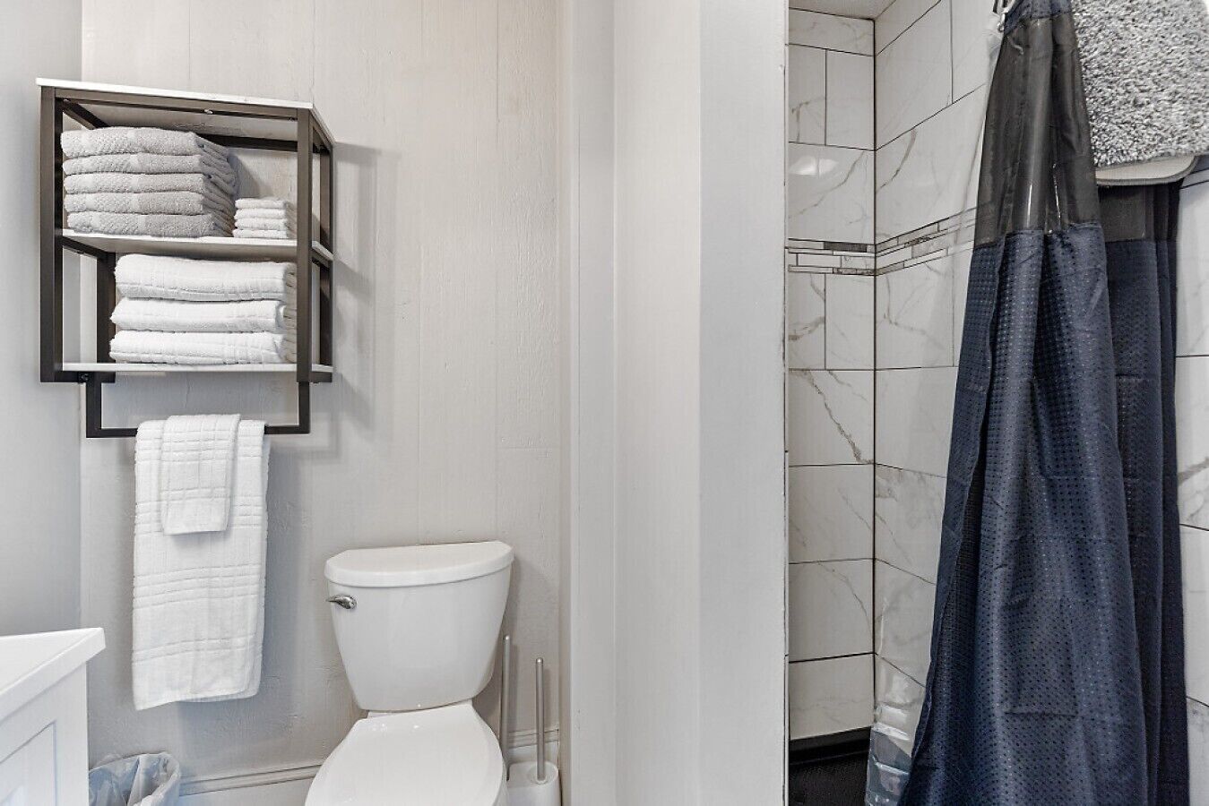 Une salle de bain comprenant des toilettes, un porte-serviettes avec des serviettes pliées et un espace douche avec un rideau de douche foncé.