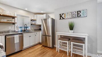 A modern kitchen with white cabinets, a stainless steel refrigerator, a wooden floor, and a bar area with stools.