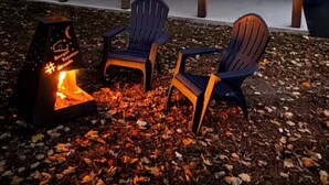 A blue house with a covered porch, three Adirondack chairs, and a fire pit.