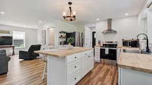 A modern kitchen with white cabinetry, a wooden island, stainless steel appliances, and a chandelier.
