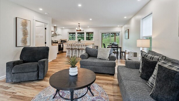 A modern living room with a grey sofa, a coffee table, and a dining area with a white table and chairs.