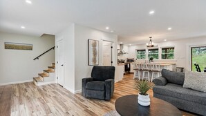 A modern living room with a staircase, a dining area, and a kitchen.