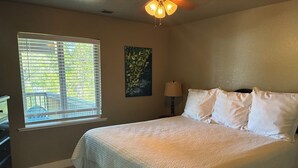 A bedroom with a large bed, a window with blinds, a painting on the wall, and a lamp beside the bed. - Bass Lake luxury cabin with lake views & boat slip (Bass Lake)