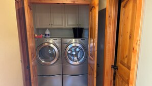 A compact laundry area with two front-loading washing machines and a cabinet above. - Bass Lake luxury cabin with lake views & boat slip (Bass Lake)