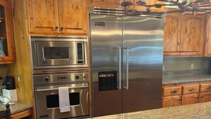 A kitchen with wooden cabinets, a stainless steel refrigerator, a microwave, and an oven. - Bass Lake luxury cabin with lake views & boat slip (Bass Lake)