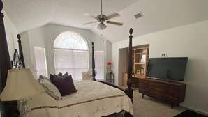 Ein Schlafzimmer mit einem Himmelbett, einem Deckenventilator, einem Fernseher, einem Schreibtisch und einem Stuhl.
