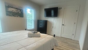 A bedroom with a bed, a TV mounted on the wall, and a window with blinds.