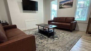 A living room with a brown sofa, a coffee table, a flat-screen TV, and a patterned rug.