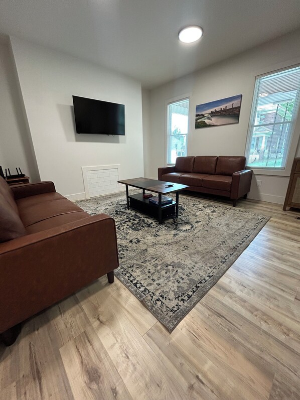 A living room with a brown sofa, a coffee table, a flat-screen TV, and a patterned rug.