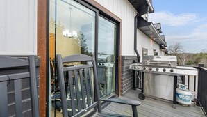 Eine Terrasse mit Grill und Propangasflasche, eine Glastür, die zu einem Raum führt, und ein Holzzaun.