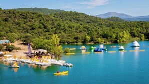 Um lago com barcos, um cais e uma colina arborizada ao fundo.