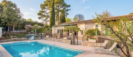 A swimming pool with a stone deck, surrounded by a fence and trees.