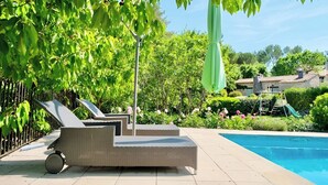 Ein Poolbereich mit Korlounge, kleinem Tisch und grünem Sonnenschirm.