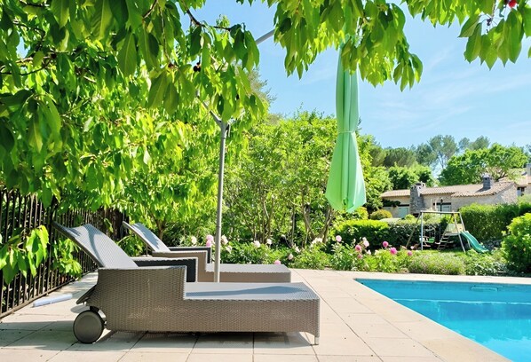 A poolside area with a wicker lounge chair, a small table, and a green umbrella.
