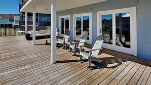 En overdækket terrasse med trægulv, hvide Adirondack-stole og store vinduer.