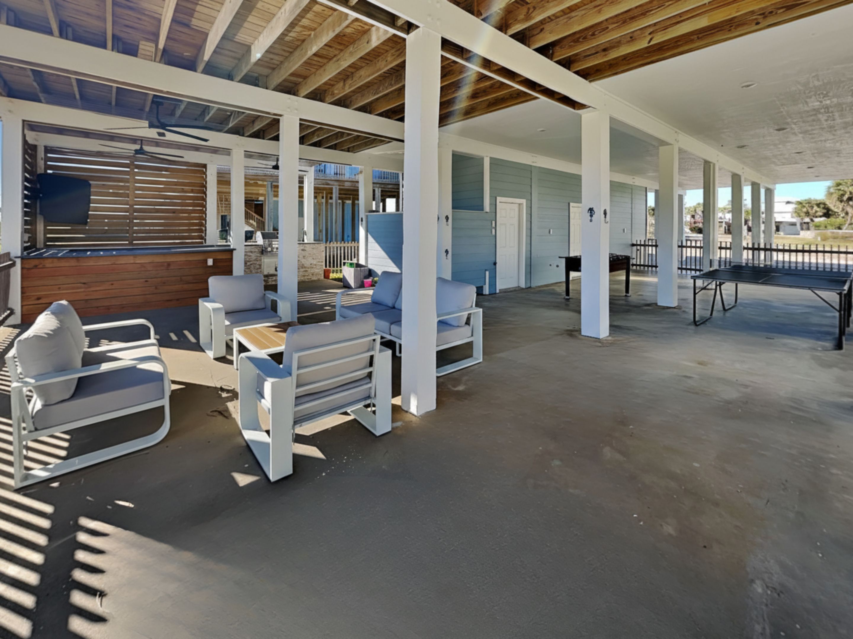 A covered outdoor area with white furniture, a ping pong table, and a view of a building with blue siding.