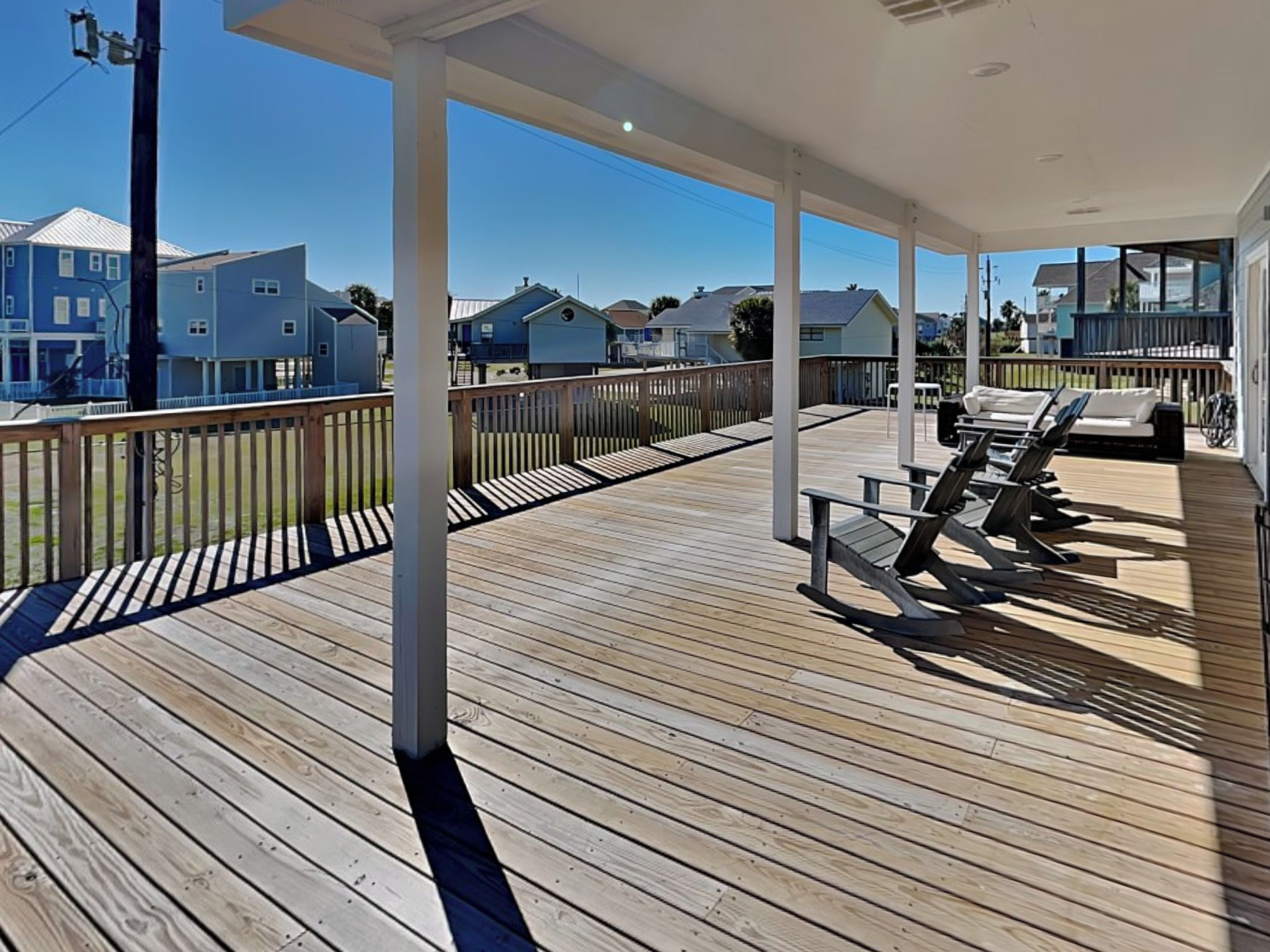 A wooden deck with lounge chairs and a covered area, overlooking a residential neighborhood.