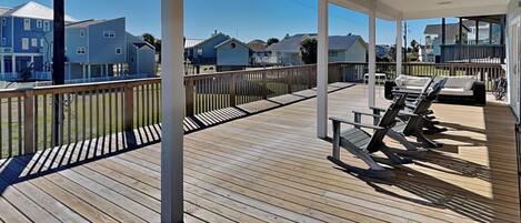 A wooden deck with lounge chairs and a covered area, overlooking a residential neighborhood.