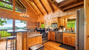 Cocina de cabaña de madera con una isla grande, electrodomésticos de acero inoxidable y vistas al exterior.