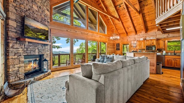 Una amplia sala de estar con chimenea de piedra, ventanas grandes, techo de madera y un rincón de descanso acogedor.