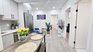 Cozinha moderna com ilha central, sala de jantar com sofá azul e sala de estar com televisão.