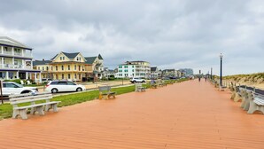 A boardwalk with benches, a grassy area, and buildings in the background. - Walk to Downtown & Beach: Ocean Grove Apartment! (Ocean Grove)