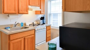 A kitchen with wooden cabinets, a white stove, a sink, and a window with blinds. - Walk to Downtown & Beach: Ocean Grove Apartment! (Ocean Grove)
