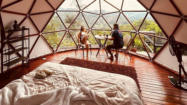 A geodesic dome room with a bed, a table, and chairs, offering a view of the outdoors. - Resurreeccion (San Francisco)
