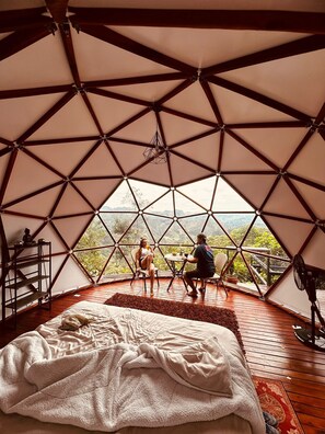 A geodesic dome room with a bed, a table, and chairs, offering a view of the outdoors. - Resurreeccion (San Francisco)