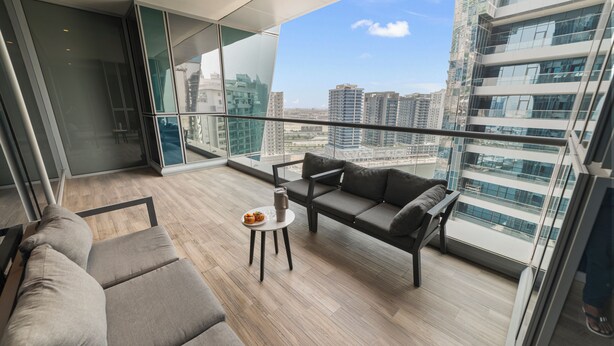 A modern balcony with a sofa, a small table, and a view of high-rise buildings. - Blissful Sanctuary 1BR Balcony w/ Canal View in vibrant Downtown Dubai (Dubai)