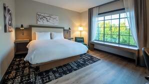 Quarto de hotel moderno com uma cama grande, duas mesas de cabeceira, uma escrivaninha e uma janela com cortinas.