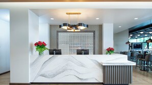 Uma área de recepção moderna com balcão de mármore, duas cadeiras, uma parede decorativa e um espaço de bar ao fundo.