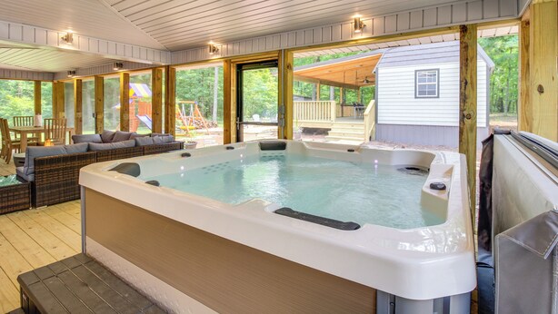 Un bain à remous situé dans un espace extérieur abrité, doté d’une terrasse en bois et offrant une vue sur une maison.