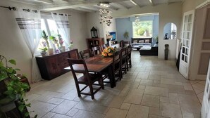 Ein geräumiger Essbereich mit Holztisch und Stühlen, eine Küchenzeile mit Schränken und Spüle sowie ein Blick auf einen Garten durch ein Fenster.