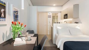 Una camera d'albergo moderna con un letto, una scrivania con una sedia, un tavolo da pranzo e un angolo cottura.