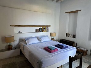 A bedroom with a bed, bedside lamps, a shelf with photos, and a wooden headboard.