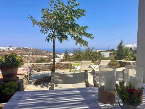 A terrace with a view of the sea, a table with a striped tablecloth, and potted plants.
