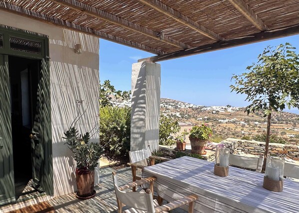 An outdoor patio with a table and chairs, potted plants, and a view of a hillside town.