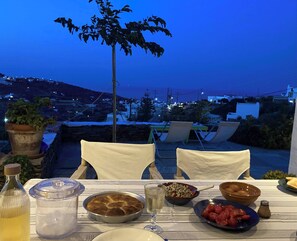 A table set for dinner with a view of a coastal town at dusk.