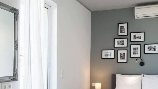 A hotel room with a bed, a chair, a bedside table with a lamp, and a wall with framed pictures.