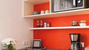 A compact kitchenette with a microwave, coffee maker, and storage shelves.