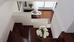 A modern interior with a wooden staircase, a white wall, and a small table with a vase of flowers.