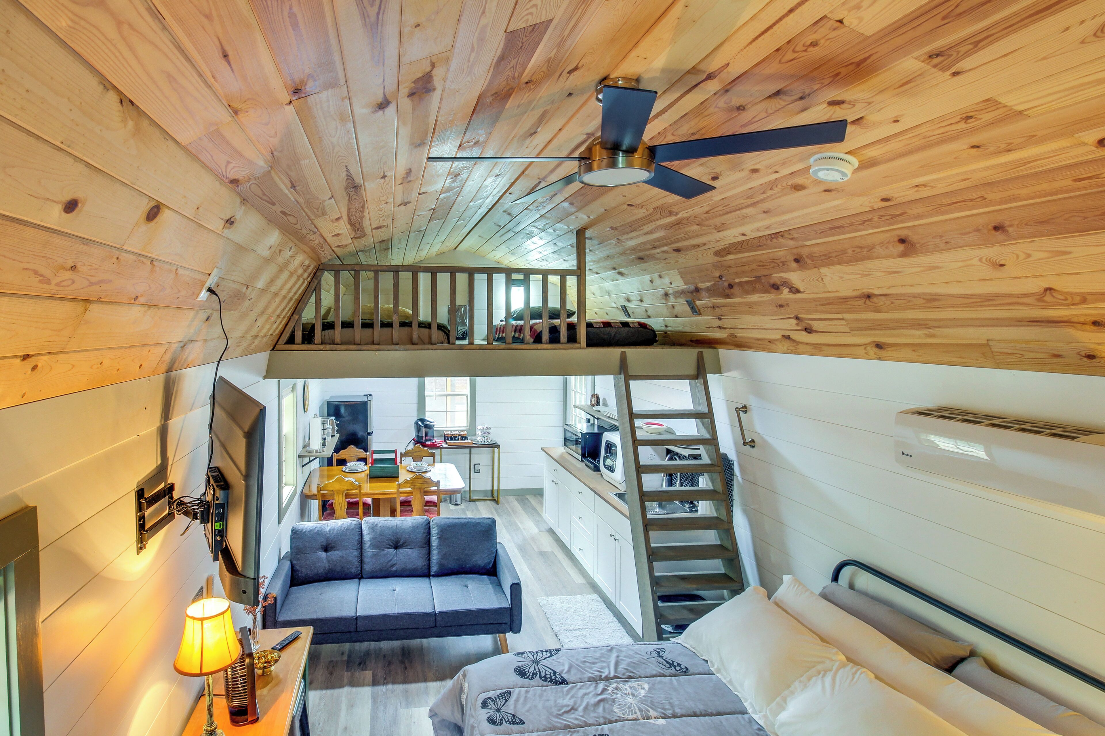 Een slaapkamer in loftstijl met een houten plafond, een plafondventilator, een stapelbed, een bureau en een kitchenette.
