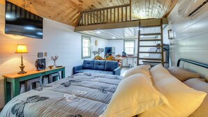 Ein Schlafzimmer mit Schlafboxbett, Schreibtisch mit Lampe, Ventilator und blauem Sofa.