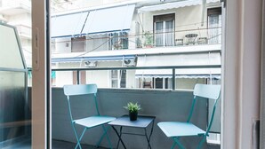 A balcony with two turquoise chairs and a small table, a potted plant, and a view of neighboring buildings.