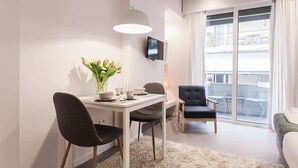 A modern hotel room with a dining area, a flat-screen TV, and a balcony with a view.