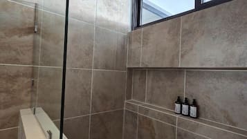 Eine Dusche mit Glasabtrennung, einer senkrechten Brause und einem Fenster darüber.