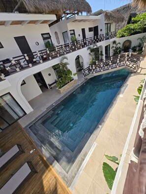 Zona de piscina con vista despejada, sillas de descanso y una estructura de techo de paja.