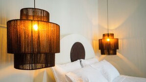 Une chambre à coucher avec un lit, du linge de lit blanc et deux lampes suspendues à l’aspect bois.